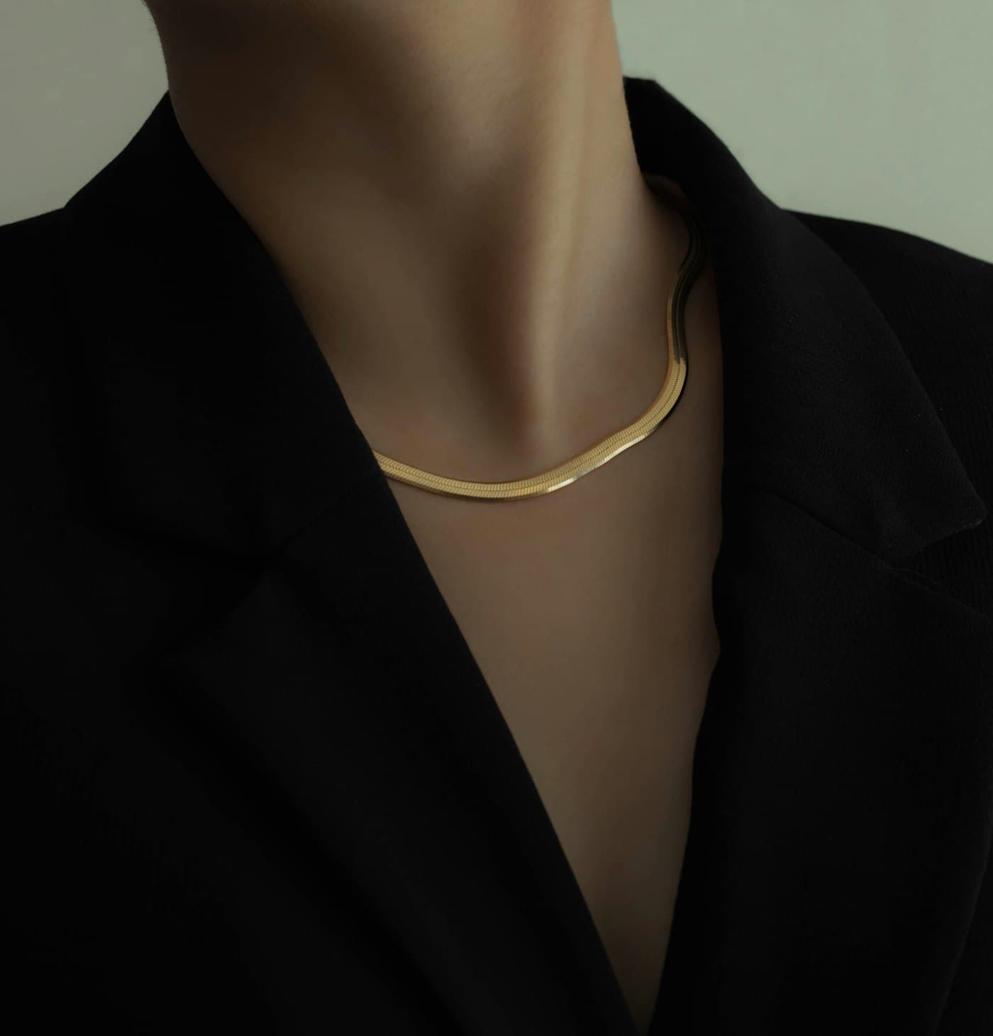 A hand-finished gold necklace by Simoni Gold, worn against a dark tailored jacket